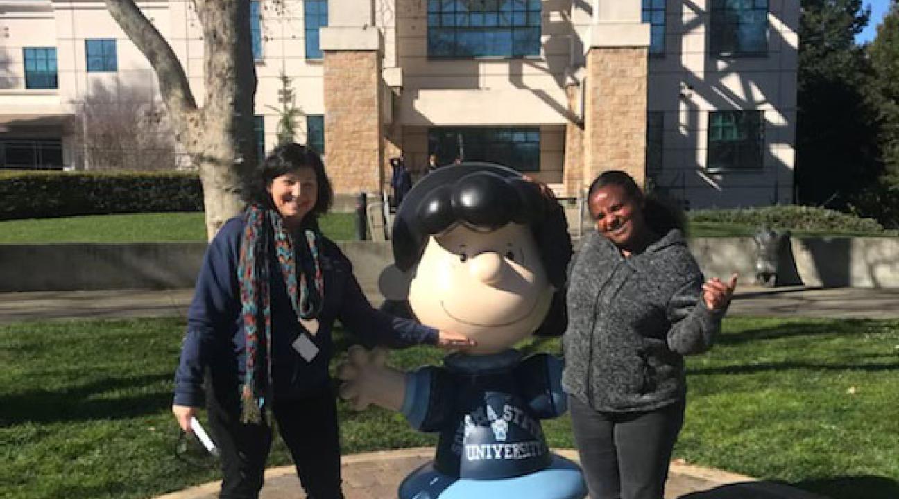 photo of two people standing next to Peanuts character Lucy statue