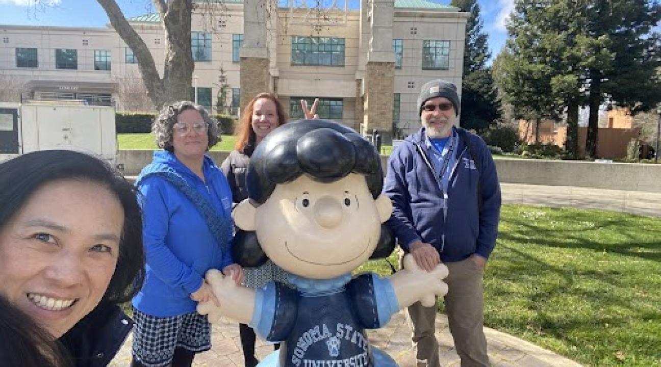 photo of 4 people surrounding statue of Peanuts character Lucy