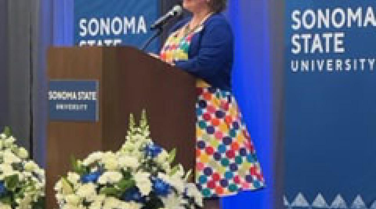 person in rainbow dotted dress speaking at podium