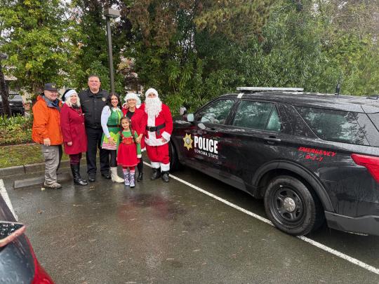 Volunteers posing with Santa Claus next to an SSUPD vehicle