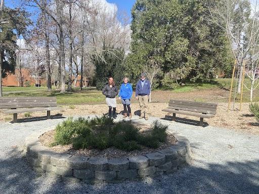 photo of three people standing between benches with greenery in front of them.