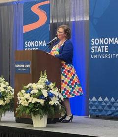 person in rainbow dotted dress speaking at podium